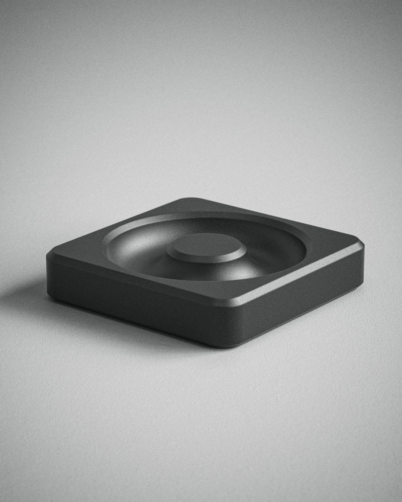 Close-up of a white tray with red speckles, placed at an angle over a similar tray in dark gray with lighter speckles. Both trays have circular indents and a textured surface.