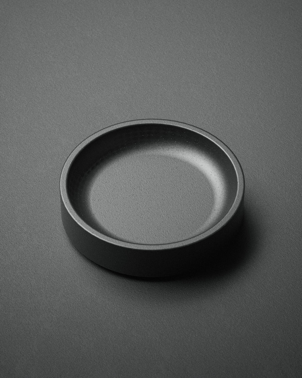 The Kuro Axis Mini is a compact, matte black circular tray shown from above on a matching textured surface with soft lighting. Ideal as a stylish desk organizer or a mini tray for small essentials.