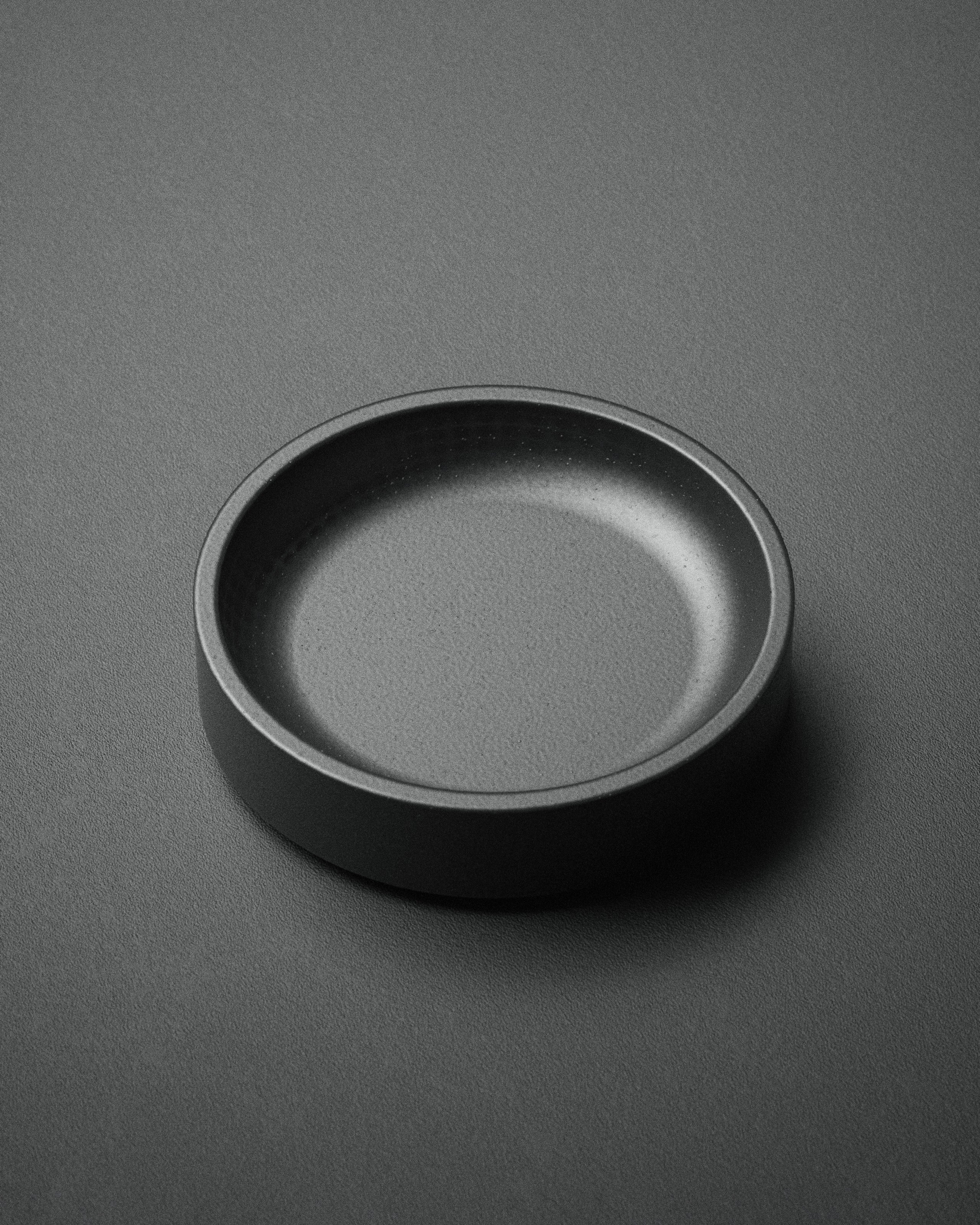 The Kuro Axis Mini is a compact, matte black circular tray shown from above on a matching textured surface with soft lighting. Ideal as a stylish desk organizer or a mini tray for small essentials.