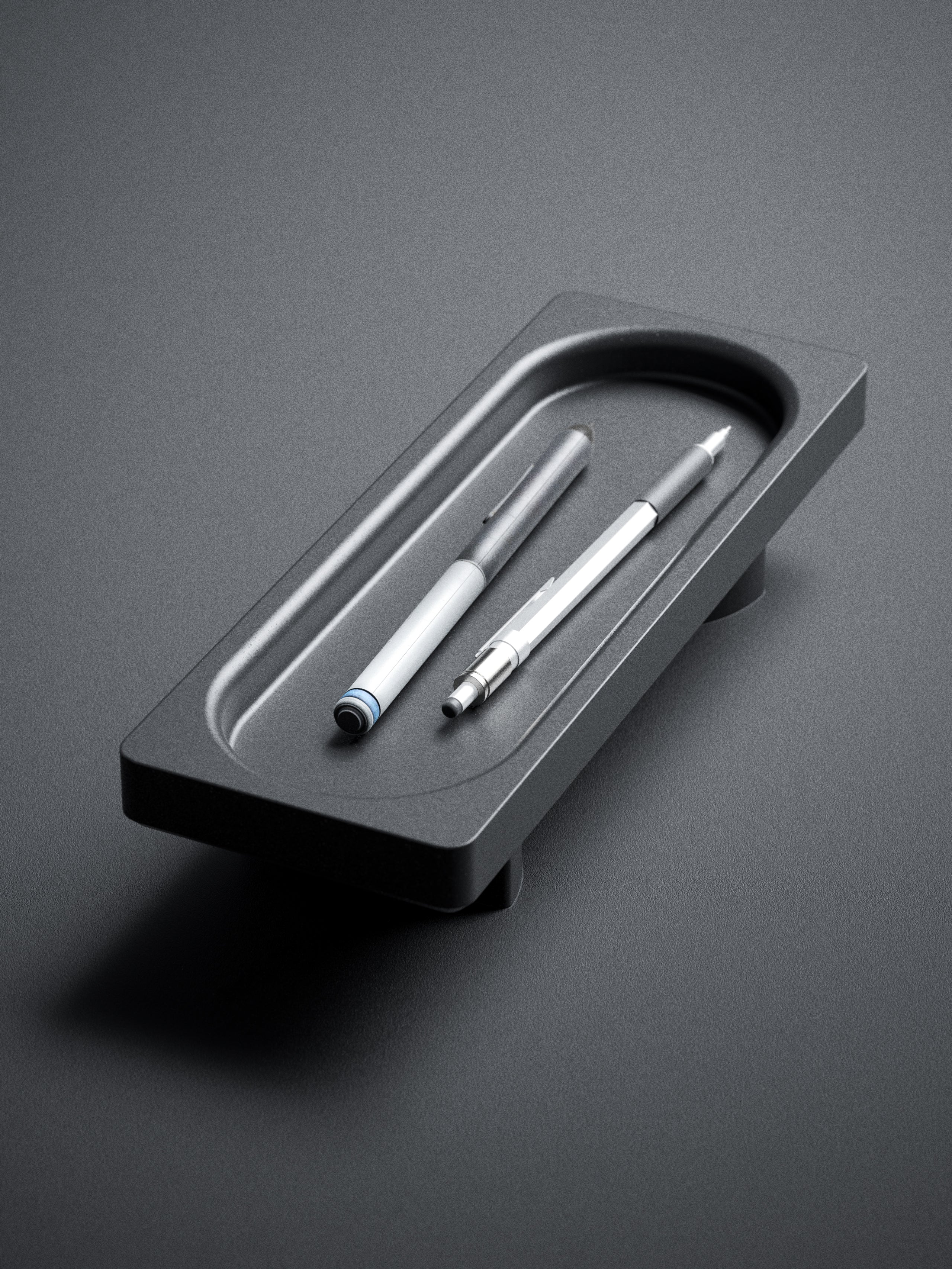 The Obsidian Rest by My Store is a minimalist black tray that holds two modern pens—one white, one silver—side by side, creating a sculptural and stylish accent for any workspace.