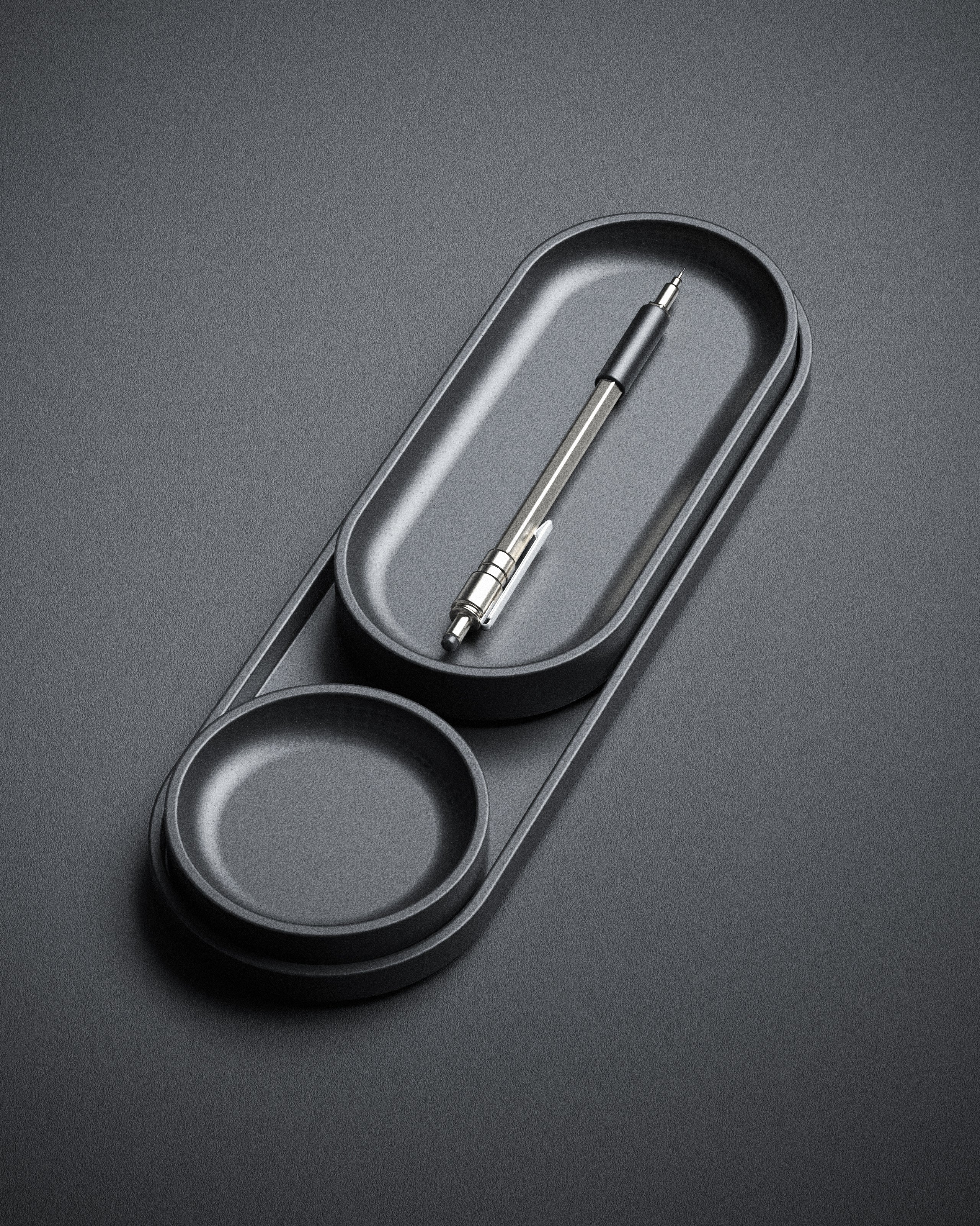 The Axis Set by My Store is a black Jesmonite minimalist desk organizer from our modular collection, with circular and oval compartments—perfect for desk trays or a black and silver pen on a dark gray surface.